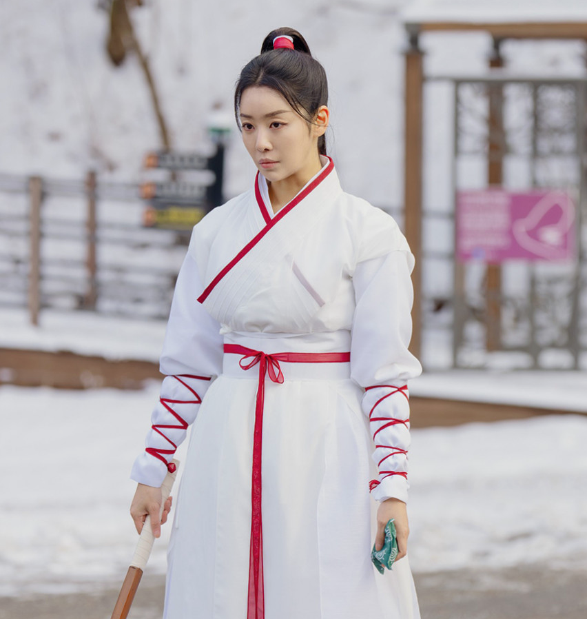 눈 내린 야외 배경에서 흰색 바탕에 붉은색 선이 들어간 사극 의상을 입고 머리를 하나로 높게 묶은 채 목검을 들고 진지하게 훈련 중인 배우 차주영의 모습