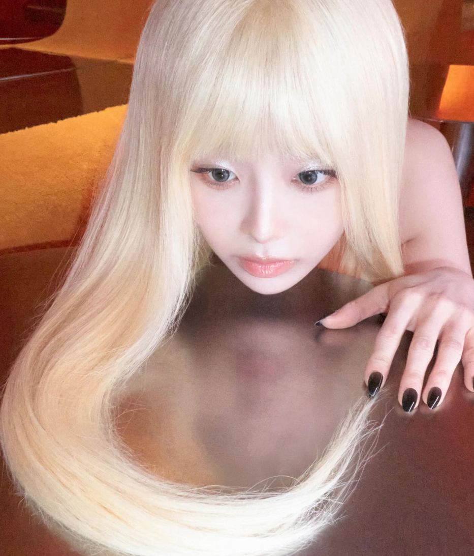 긴 금발 머리를 늘어뜨린 채 반사되는 금속판 위에 턱을 괴고 신비로운 표정으로 정면을 응시하고 있는 가수 츄의 모습