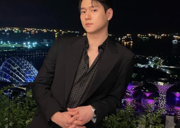 화려한 도시의 야경과 바다를 배경으로 검은색 수트와 도트 무늬 셔츠를 입고 난간에 기대어 정면을 응시하는 배우 고경표의 모습