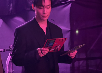 2025 멜론 뮤직 어워드(MMA) 백스테이지에서 보라색 조명을 배경으로 검은색 슈트를 입고 시상 카드를 진지하게 확인하고 있는 배우 허남준의 모습