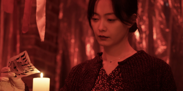 영화 ‘온리 갓 노우즈 에브리띵’에서 배우가 붉은 조명 아래 촛불을 응시하며 고뇌에 잠긴 장면.