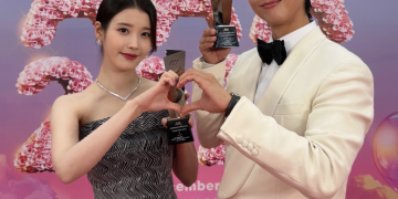 2025 아시아 아티스트 어워즈(AAA) 레드카펫 배경 앞에서 트로피를 들고 손하트를 만들고 있는 박보검과 아이유의 다정한 모습