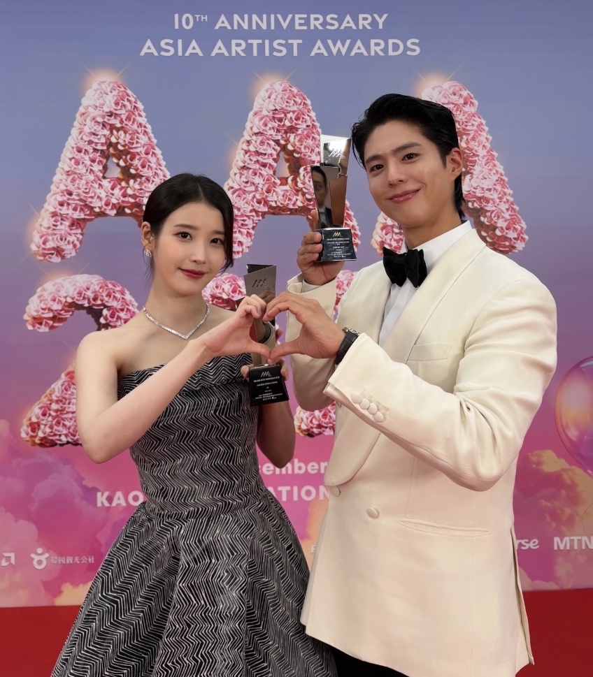 2025 아시아 아티스트 어워즈(AAA) 레드카펫 배경 앞에서 트로피를 들고 손하트를 만들고 있는 박보검과 아이유의 다정한 모습