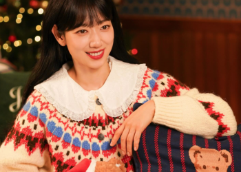 크리스마스트리와 따뜻한 조명이 가득한 배경에서 레이스 깃이 달린 노르딕 패턴 니트를 입고 곰 인형 쿠션 곁에서 밝게 웃고 있는 배우 박신혜의 모습