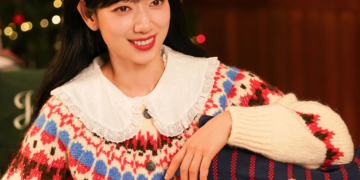크리스마스트리와 따뜻한 조명이 가득한 배경에서 레이스 깃이 달린 노르딕 패턴 니트를 입고 곰 인형 쿠션 곁에서 밝게 웃고 있는 배우 박신혜의 모습